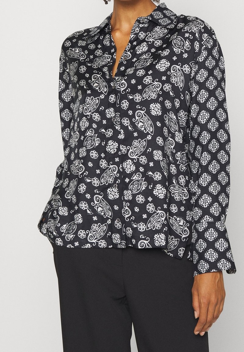 Chemise à motifs noir et blanc, présentant un design paisley et des accents floraux, avec un col à revers et une patte de boutonnage. Tissu doux.