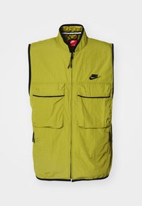 Žalias be rankovių liemenė su dviem priekinių netikro kišenių, užtrauktuku ir juodu apvadu; krūtinėje yra Nike logotipas. Rašytinis audinys.