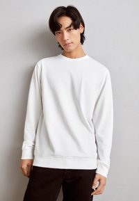 Hvid sweatshirt med lange ærmer, rund halsudskæring og ribbet manchetter. Blødt bomuldsstof med minimalistisk design og diskret logo-detalje.