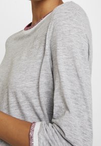 Graues Langarmshirt mit glitzerndem pinkem Ausschnitt und subtiler "Love"-Stickerei auf der Brust. Weicher, strukturierter Stoff mit lockerer Passform.