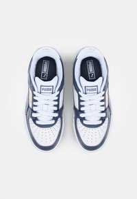 Hvide og marineblå sneakers med perforeret tå, snørret design og synlig branding på tungen og siden. Glatte læder- og stofmaterialer.
