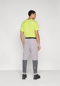 Ανδρικό φωτεινό πράσινο πουκάμισο με κοντά μανίκια και γκρι φόρμα με ribbed σκουρόχρωμες γκρι μανσέτες· μαύρη μέση και παπούτσια· λογότυπο στην πλάτη του πουκαμίσου.