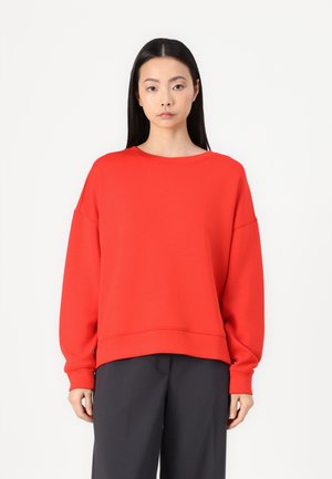 Roter übergroßer Sweatshirt mit rundem Ausschnitt und langen Ärmeln, mit einer weichen Textur und einer lockeren Passform, kombiniert mit dunklen Hosen.