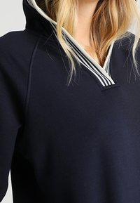 Sudadera navy con cuello a rayas en contraste. Material suave, corte relajado y presenta un diseño de media cremallera para facilitar su uso.