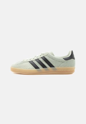 Baskets basses Adidas avec tige en mesh blanc, trois bandes noires, semelle en caoutchouc naturel et un patch noir au talon vues de côté.