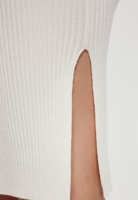 Krémový ribbed top s bočním rozparkem, vyrobený z texturované látky. Střih zvýrazňuje hladkou pleť pod ním.