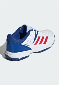 Chaussure de sport blanche avec des accents bleus, dotée de rayures rouges, de côtés perforés et d'une semelle texturée pour l'adhérence. Conçue pour la stabilité sur le court.