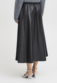 Schwarze Kunstlederrock mit elastischem Bund, A-Linien-Form und glatter Textur. Getragen mit silbernen High Heels.