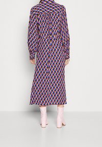 Maxikleid mit einem geometrischen Muster in Blau, Pink und Orange. Lange Ärmel und eine taillierte Taille. Kombiniert mit hellrosa Ankle Boots.