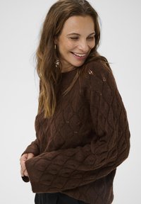 Brown knitted sweater with a textured diamond pattern, featuring wide sleeves and a round neckline. Soft, cozy material with a loose fit.