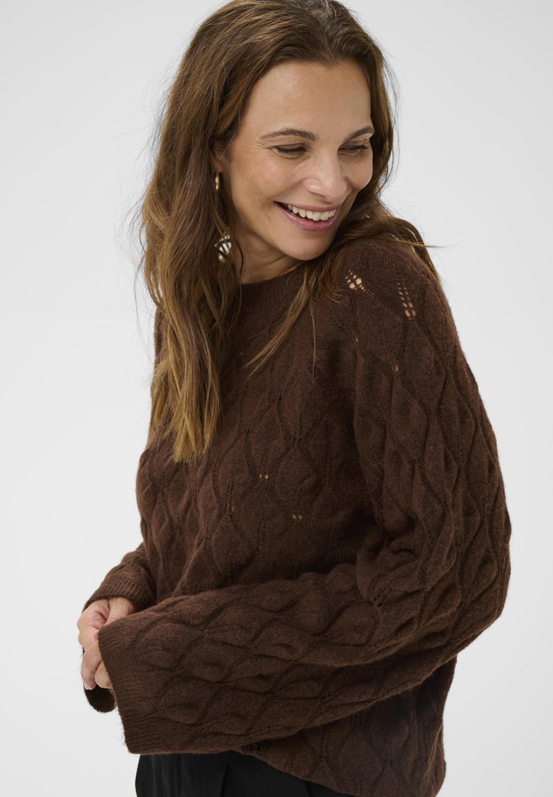 Brown knitted sweater with a textured diamond pattern, featuring wide sleeves and a round neckline. Soft, cozy material with a loose fit.