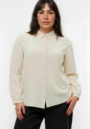 Chemise crème à boutons, avec des rayures verticales discrètes, à manches longues et avec un col. Le tissu semble soyeux avec une texture lisse.