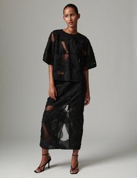 Σετ από μαύρο δίχτυ με τοπ και φούστα με υφασμένα κυματιστά σχέδια. Διαφανές ύφασμα με άνετη εφαρμογή. Μαύρες ψηλοτάκουνες πέδιλες με λουράκια ολοκληρώνουν την εμφάνιση.