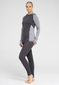 Hættegrå træningstrøje med lange ærmer og tommelhuller, kombineret med mørke tights. Begge stykker tøj har en tætsiddende pasform og en glat overflade.