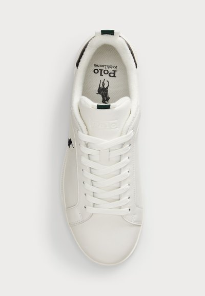 Bijele kožne tenisice s okruglim prstima, vezanjem sprijeda, zelenim naglaskom na peti i crnim logom na jeziku i sa strane. Teksturirana površina.