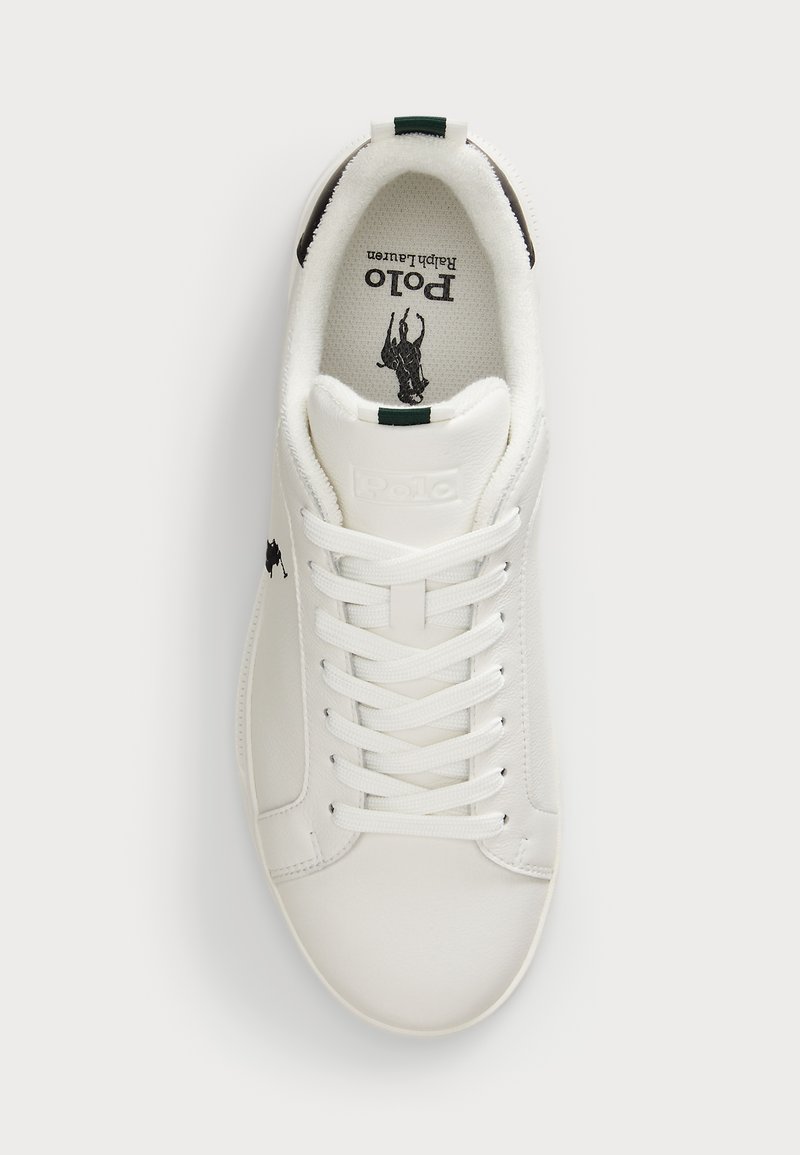 Sneaker in pelle bianca con punta rotonda, chiusura con lacci, dettaglio verde sul tallone e logo nero sulla linguetta e sul lato. Superficie texture.