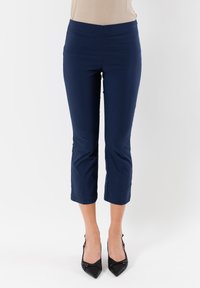 Pantaloni blu navy a vita alta con una superficie liscia e una fascia elastica, caratterizzati da una vestibilità sartoriale e che terminano poco sopra la caviglia.