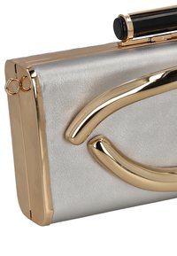 Metallische silberne Clutch mit glatter Textur, versehen mit einem goldakzentuierten, geschwungenen Design und einem schwarzen oberen Verschluss. Kompakte, rechteckige Form.