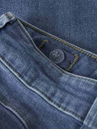 Tissu en denim bleu foncé avec un tissage texturé, présentant des coutures jaunes et une fermeture à bouton avec un motif floral sur la surface du bouton.