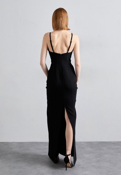 Black, form-fitting evening dress featuring thin straps, a back zipper, and a high slit on the left side. Smooth fabric with a sleek silhouette.