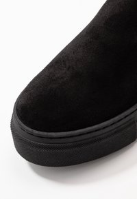 Botín de ante negro a la muñeca con punta redonda y suela de goma texturizada. Presenta un acabado suave con acentos texturizados en contraste.