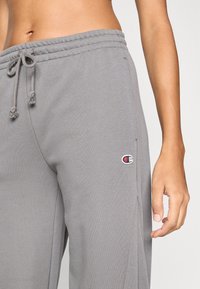 Γκρι φόρμες από μαλακό ύφασμα, με ελαστική ζώνη μέσης και κορδόνι, πλαϊνές τσέπες και ένα μικρό κεντημένο λ ογότυπο.