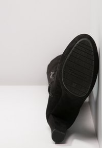 Czarne zamszowe botki za kostkę z płaską podeszwą, teksturowaną gumową podeszwą oraz bocznym zamkiem błyskawicznym. Prezentują gładką cholewkę i okrągły nosek.