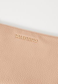 Bežinė odinė rankinės, turinti tekstūruotą paviršių, su auksiniu „VALENTINO“ logotipu įspaudžiamu viršuje.
