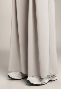 Brede, lichtgrijze stoffen broek met een gladde textuur, gecombineerd met witte en grijze sport sneakers met een dikke zool en mesh accenten.