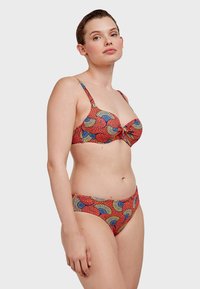 Bikini rouge avec un motif de fans en bleu et jaune. Haut de style bralette avec des bretelles réglables, bas taille basse assortis. Texture lisse.