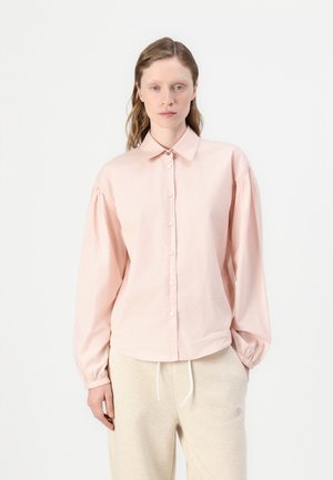 Light pink button-up shirt with long sleeves, gathered shoulders, and a collar. Made from a soft fabric with a subtle sheen and minimal logo detail.