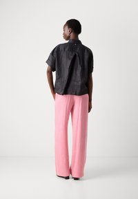 Camicia nera in lino a maniche corte con piega posteriore, abbinata a pantaloni rosa chiaro a gamba larga con finitura testurizzata. Calzature nere e orecchini a cerchio.