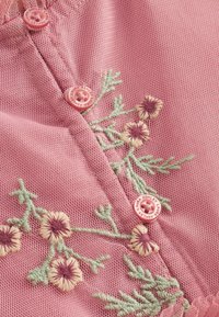 Tissu en maille rose avec broderie florale en vert et crème, avec trois boutons roses étiquetés "Laura Ashley."