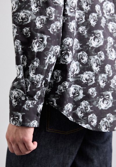 Black and gray long-sleeve shirt with rose pattern, featuring a buttoned cuff and a curved hem. Fabric appears smooth and lightweight.