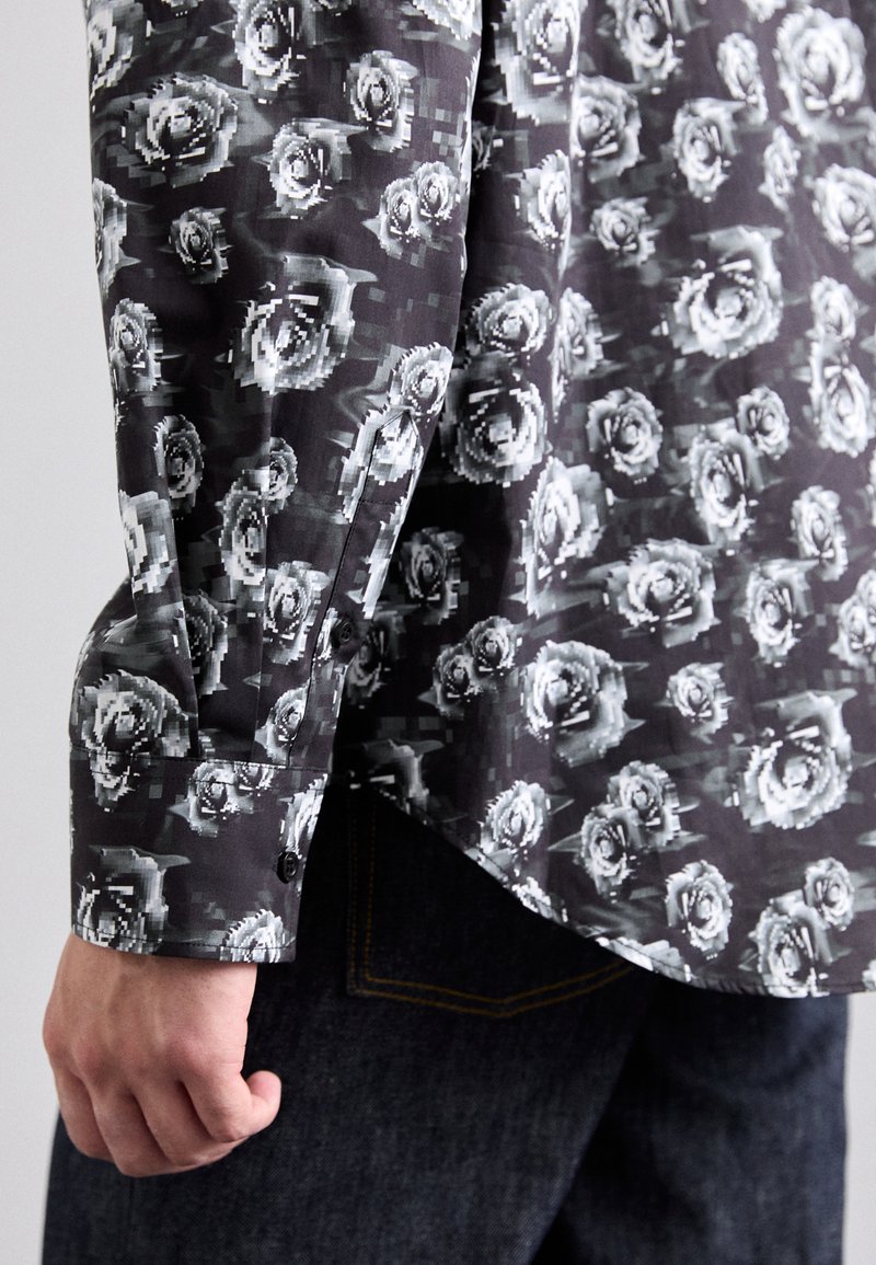 Schwarz-graues Langarmshirt mit Rosenmuster, ausgestattet mit einem knöpfbaren Bündchen und einem abgerundeten Saum. Der Stoff wirkt glatt und leicht.