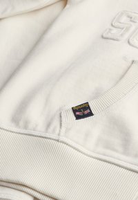 Crème katoenen sweatshirt met geborduurd "S", geribde manchetten en een zijpatch met vlaggraphics en "Superdry" branding.