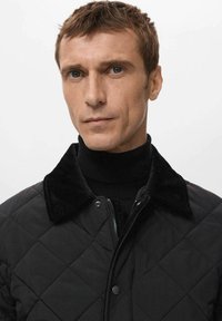 Giacca nera trapuntata con collo in velluto a coste e chiusure a scatto. Presenta una zip frontale e un tessuto strutturato per maggiore calore.