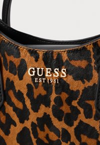 Tasje met luipaardprint en glanzende zwarte afwerking. Voorzien van het gouden "GUESS EST 1981" logo. De vachtstructuur voegt diepte toe aan het oranje en zwarte patroon.