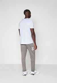 Witte T-shirt met korte mouwen, grijze afgezakte joggingbroek met witte chevronpatronen, zwart-witte sportschoenen. Glad stoftextuur.