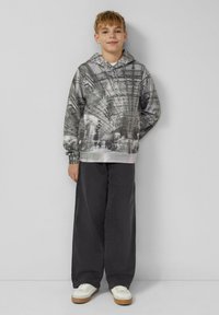 Felpa con cappuccio in scala di grigi con design fotografico; maniche lunghe, polsini e orlo a costine. Abbinata a pantaloni neri a gamba larga e sneakers bianche.