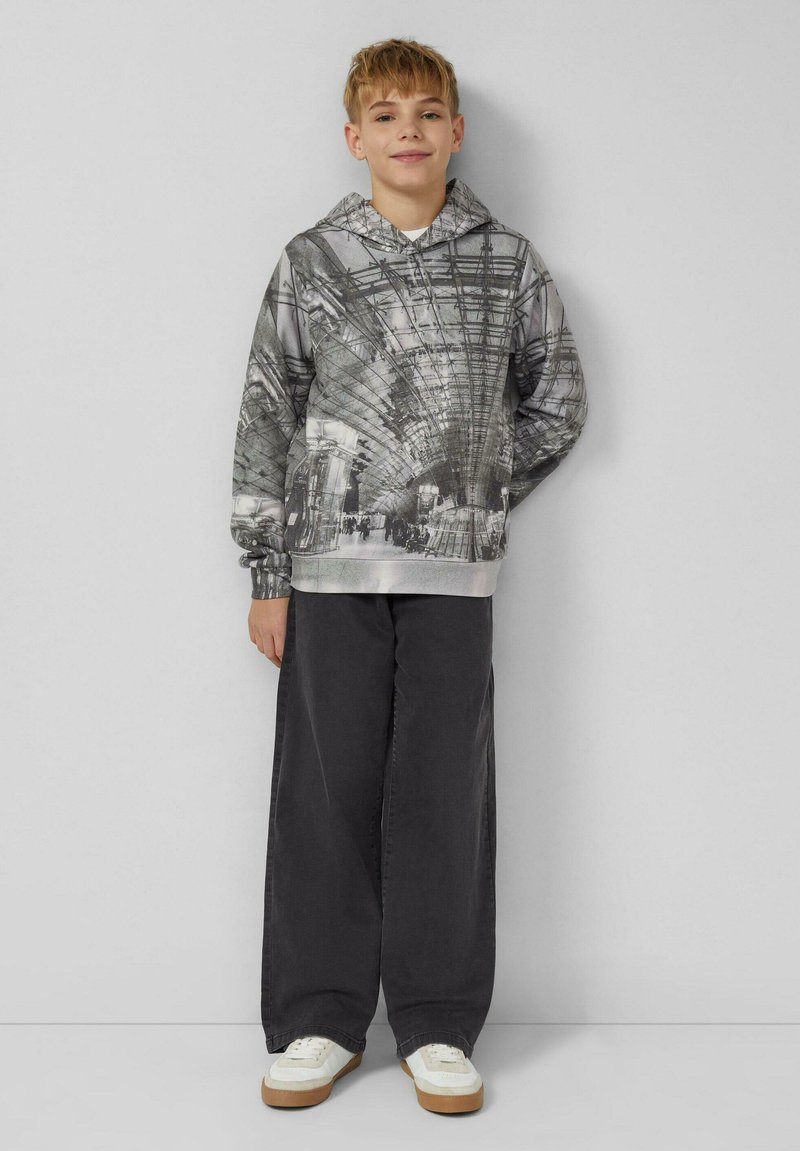 Felpa con cappuccio in scala di grigi con design fotografico; maniche lunghe, polsini e orlo a costine. Abbinata a pantaloni neri a gamba larga e sneakers bianche.