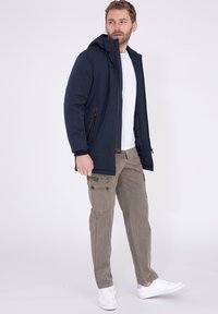 Marineblaues Kapuzenjacke mit einer Reißverschlusstasche, kombiniert mit hellbraunen Cargo-Hosen und weißen Sneakers. Glattes Material mit modernem Schnitt.