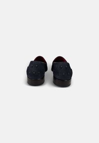 Zapatos de ante en color marino con acentos negros en forma de diamante, talones redondeados y una suela oscura. El interior es rojo, con una textura suave.