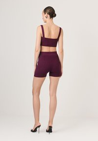 Burgundi bordázott kötött melltartó és rövidnadrág szett. A bralette széles pántokkal rendelkezik, a rövidnadrág pedig magas derékkal és feszes szabással készült. A magassarkúk feketék.