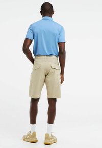 Lichtblauwe polo met korte mouwen, gecombineerd met khaki cargoshorts met twee achterzakken, gedragen met beige sneakers en witte sokken.