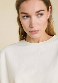 Sweatshirt beige clair avec un col rond, texture en coton doux et coupe décontractée, présentant un design minimaliste sans motifs visibles.