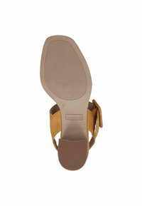 Sandal con tacco quadrato in suede beige, con suola testurizzata e cinturino largo. Presenta un logo del marchio sulla suola e una fibbia regolabile.