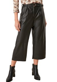 Černé faux kožené kalhoty culottes s vysokým pasem, obsahující odpovídající pásek, puky a zkrácenou délku, spojené s černými kotníkovými botami.