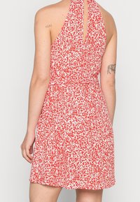 Robe dos nu à motifs rouges et blancs avec une ouverture en forme de goutte d'eau dans le dos, taille cintrée et jupe fluide. Tissu léger avec une texture lisse.