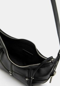 Čierna kožená crossbody taška s uzáverom na zips, interiérovou podšívkou a striebornými kovovými prvkami. Zakrivený tvar s detailmi prešívania.